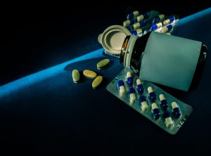 Pills and opened cap medicine bottle with blank label on dark blue background with copy space. Tablets and capsules. Pharmaceuticals industry. Vitamins and supplements.